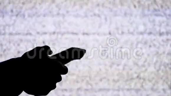 一只手拿着电视遥控器在电视屏幕背景上的剪影带有白色的静态噪音视频的预览图