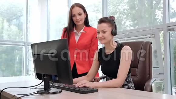 两位年轻妇女在电脑前的一间明亮的办公室里工作讨论工作流程并享受成功的交易头和头视频的预览图