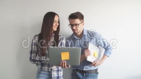 快乐的混血情侣在灰色的墙壁背景下一边站着一边拿着笔记本电脑一边庆祝孤立的生活视频的预览图