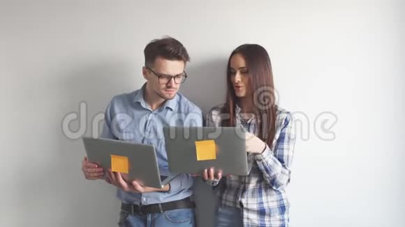 快乐的混血情侣在灰色的墙壁背景下一边站着一边拿着笔记本电脑一边庆祝孤立的生活视频的预览图