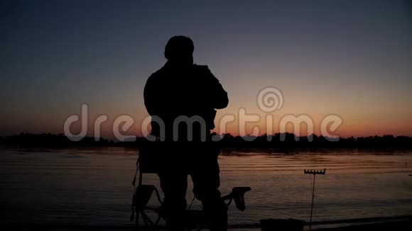 渔夫的剪影在河里扔鱼竿坐在椅子上视频的预览图