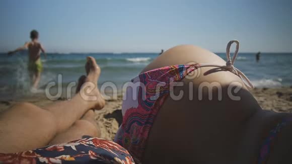 年轻的白种人男人和女人白天躺在靠近大海的沙滩上观点一个男孩跑到海里视频的预览图