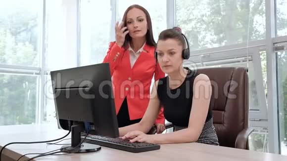 两位年轻妇女在电脑前的一间明亮的办公室里工作讨论工作流程并享受成功的交易头和头视频的预览图