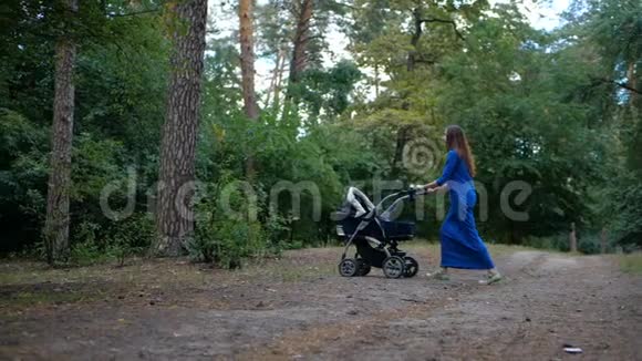 年轻妈妈和婴儿车在森林里散步慢动作视频的预览图