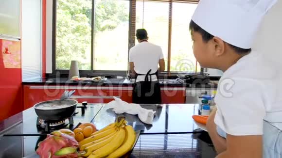泰国私人厨师做饭他的小儿子戴着厨师帽子坐在桌子上有一个现代风格的家庭厨房视频的预览图