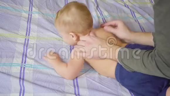 父亲带着婴儿在床上按摩身体健康的生活方式慢动作视频的预览图
