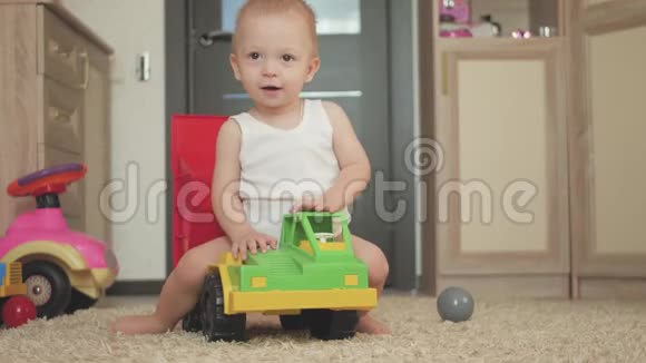 可爱的小男孩在家里地板上玩一个大汽车玩具小孩子在室内玩玩具车未来司机视频的预览图