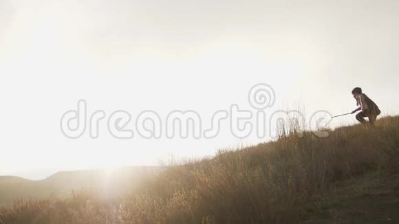 一个拿着木剑的男孩带着太阳在山顶上奔跑到地平线上视频的预览图