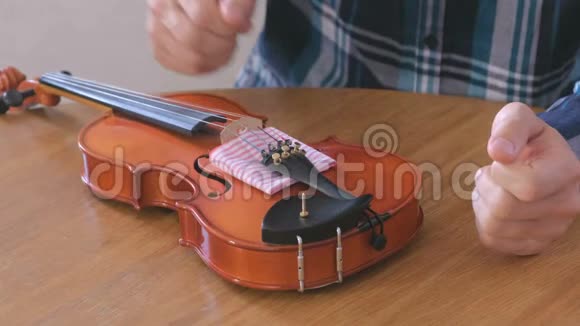 穿格子衬衫的年轻人的特写双手正在修理坐在桌子旁的小提琴拧紧螺栓就位视频的预览图