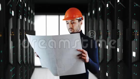一个戴着安全头盔的英俊男子在后台阅读带有大型系统服务器的蓝图视频的预览图
