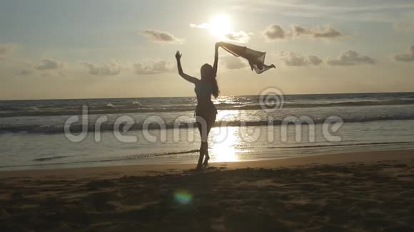 日落时分带着围巾的年轻快乐的女人沿着海边散步喜欢夏天的女孩比基尼女性剪影视频的预览图