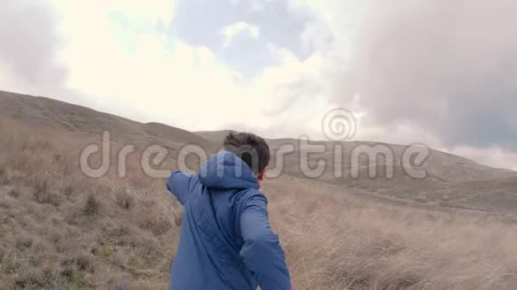 一个带着高草的男孩跑向地平线和小山慢速视频视频的预览图