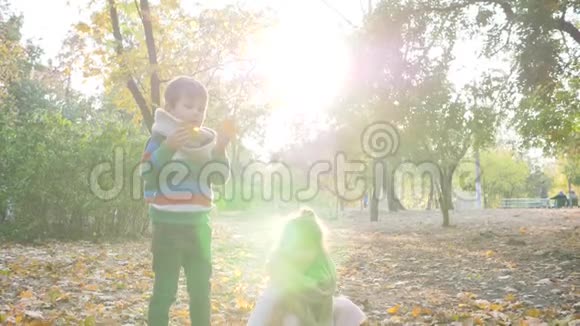 快乐的孩子们在公园里把黄叶扔到空中在树的背景上玩背光游戏视频的预览图