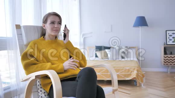 年轻女子在椅子上放松时用电话交谈视频的预览图