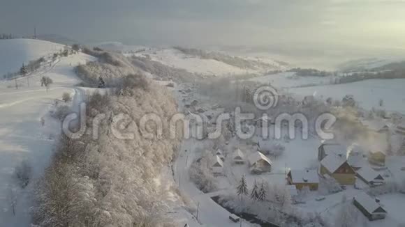 日出时飞越喀尔巴阡山的一个村庄高山积雪房屋的鸟瞰图视频的预览图