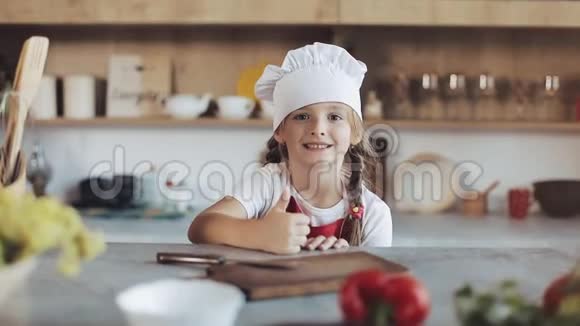 厨房里一个可爱的小女孩打扮成专业厨师的肖像看着镜头微笑她是视频的预览图