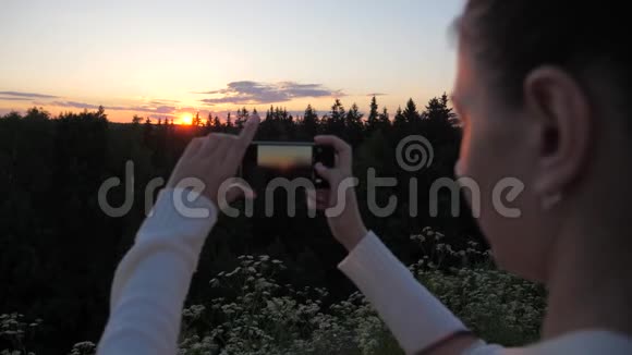 女孩用智能手机拍摄和拍照日落视频的预览图