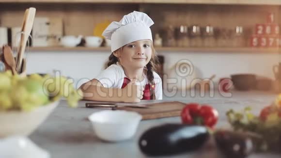 厨房里一个可爱的小女孩打扮成专业厨师的肖像看着镜头微笑她是视频的预览图