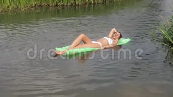 在床垫上漂在河里的白比基尼漂亮的晒黑女人视频的预览图