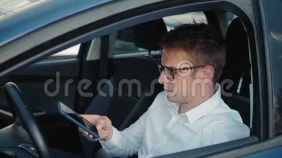 一个快乐的男人坐在车里用智能手机语音识别功能在户外的一个背光公园里视频的预览图