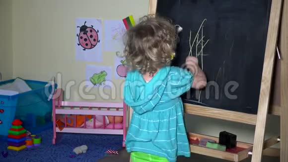 可爱的蹒跚学步的女孩在家画黑板视频的预览图
