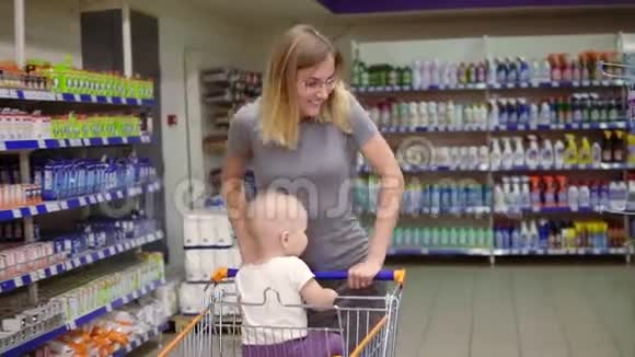 年轻的母亲正推着手推车向前走可爱的孩子坐在购物车里小宝宝和她妈妈视频的预览图