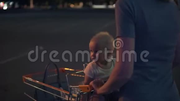小婴儿坐在一辆购物车里而她的母亲正推着购物车向前走走在路边的停车场视频的预览图