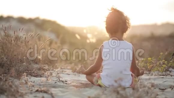 穿着白衬衫的小女孩坐在沙滩上沉思日落视频的预览图