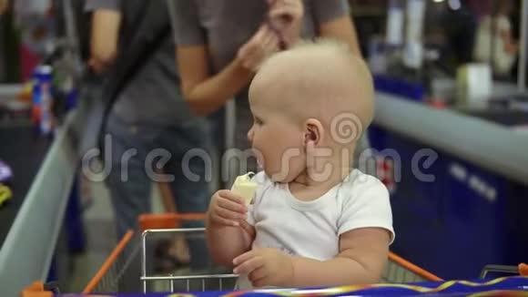 一个可爱的小婴儿吃香蕉坐在购物车里而她的母亲正在从视频的预览图
