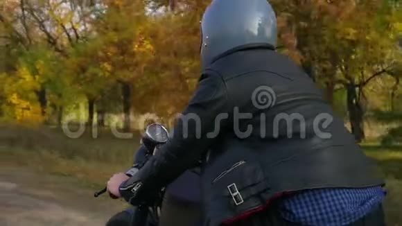 阳光明媚的一天一名身穿灰色头盔皮夹克和格子衬衫的男子骑摩托车在柏油路上视频的预览图