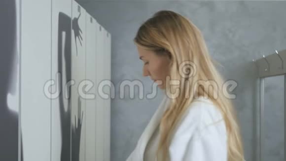 穿浴袍的女人从更衣室的橱柜里拿电话视频的预览图