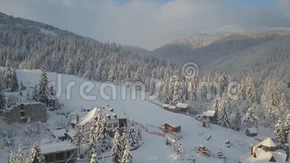 飞越喀尔巴阡山脉和一个村庄的滑雪场鸟瞰群山中白雪覆盖的房屋农村视频的预览图