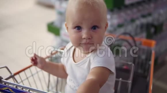 小婴儿坐在超市的购物车里等着她的父母去购物带着家庭购物视频的预览图