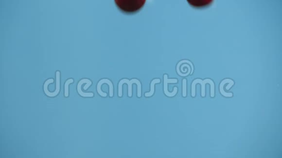 两颗樱桃在蓝色背景下缓慢地落入水中视频的预览图