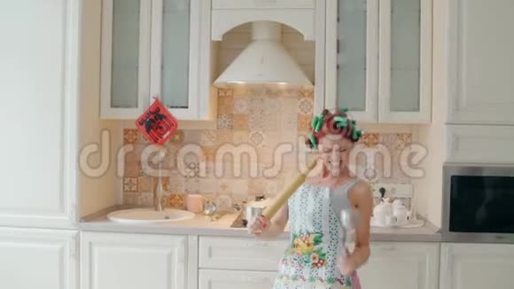 有趣的女人在家厨房做饭时用擀面杖跳舞唱歌视频的预览图