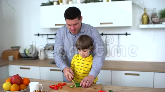 父亲教儿子在家里的厨房里切蔬菜切黄瓜慢动作幸福的家庭视频的预览图