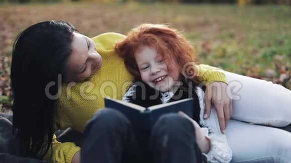 妈妈和她的小女儿坐在秋天的部分读了一本书他们说得很好秋天森林里的幸福家庭视频的预览图