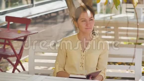 奇妙的秋景一位迷人的年轻女子坐在街头咖啡馆的桌子旁开心地笑着视频的预览图