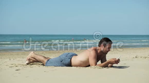 年轻人拿着手机躺在海边的海滩上视频的预览图