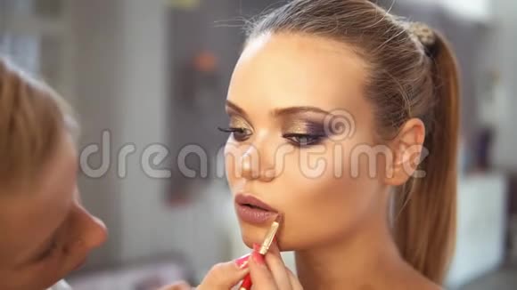 专业化妆师用特殊的画笔将口红涂在白种人模型上的特写镜头唇唇视频的预览图