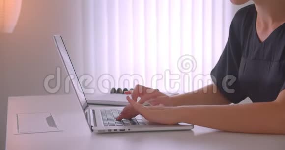 戴着眼镜的年轻白种人女商人的特写照片她用笔记本电脑看着相机在办公室里开心地笑着视频的预览图