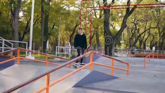 年轻的极限滑板运动员听着音乐在耳机磨下栏杆在溜冰场慢镜头视频的预览图