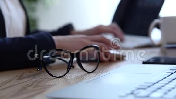 办公室现场有笔记和试卷一支笔和一副眼镜一个年轻的女人她的手在电脑上工作视频的预览图