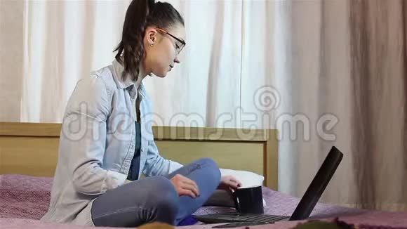 一个年轻漂亮的女孩从她的笔记本电脑工作同时喝咖啡从一个黑色的杯子视频的预览图