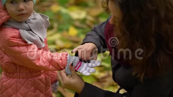 妈妈在秋天公园给小女孩穿上暖和的衣服慢动作视频的预览图
