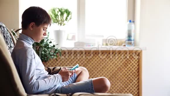 男孩坐在房间的地板上用智能手机现代技术在儿童生活中的理念视频的预览图