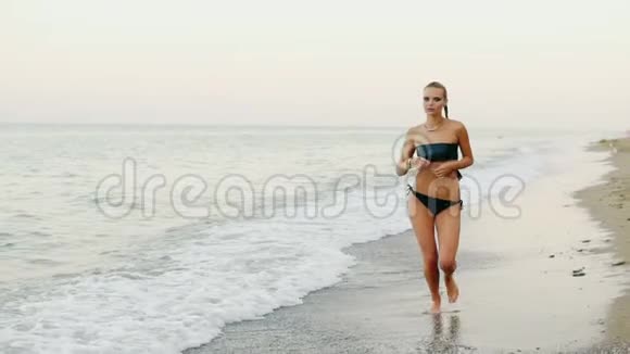 年轻迷人的女人穿着黑色皮衣在海滩上海边奔跑她的马尾辫在风中飘扬视频的预览图