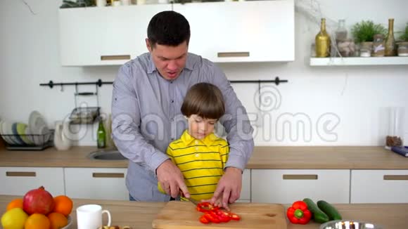 父亲教儿子在家里的厨房里切蔬菜切胡椒粉慢动作幸福的家庭视频的预览图