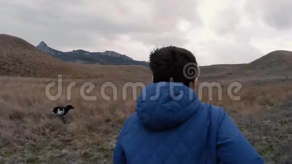 一个男孩带着一只狗在雨中跑过田野跑到山上视频的预览图