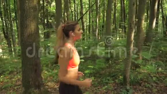 运动可爱的女人戴着耳机在路上奔跑森林侧视视频的预览图